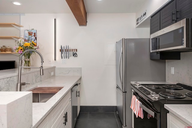 kitchen with white cabinets, stainless steel appliances, light stone counters, and dark tile patterned floors