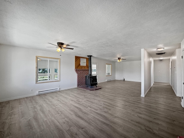 unfurnished living room with ceiling fan, plenty of natural light, hardwood / wood-style flooring, and a wood stove