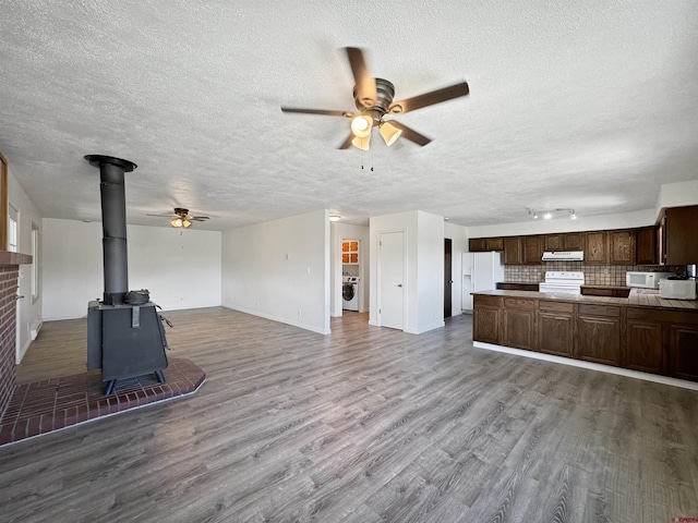 unfurnished living room featuring washer / clothes dryer, wood finished floors, a wood stove, and a ceiling fan