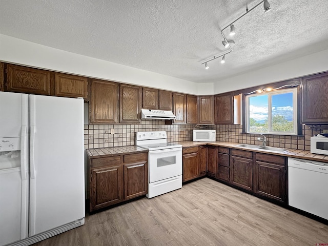 kitchen with white appliances, a sink, under cabinet range hood, and tile countertops