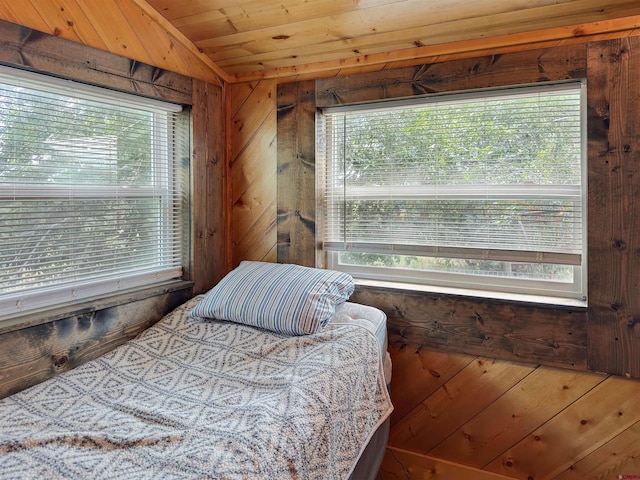 bedroom with vaulted ceiling, wooden ceiling, multiple windows, and wood walls