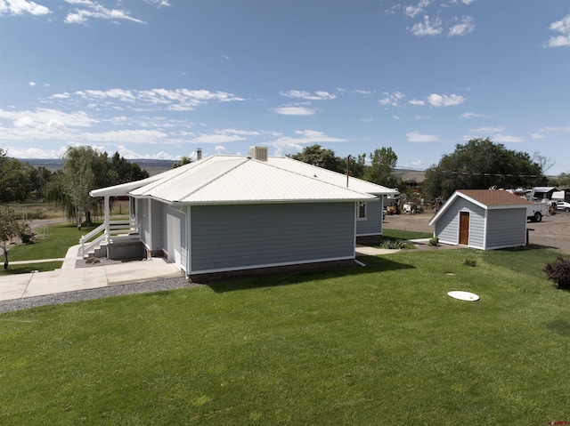 view of side of property featuring central air condition unit, metal roof, a lawn, and an outbuilding