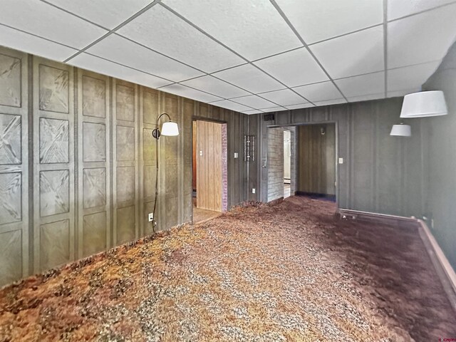 basement featuring wood walls, a drop ceiling, and carpet floors