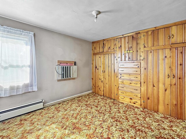 carpeted empty room featuring wood walls and baseboard heating