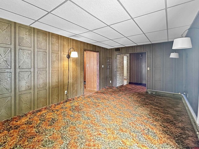 basement featuring a drop ceiling, wood walls, and carpet