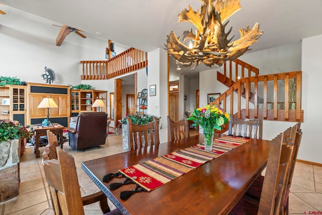 tiled dining area with stairway, baseboards, a high ceiling, and ceiling fan with notable chandelier