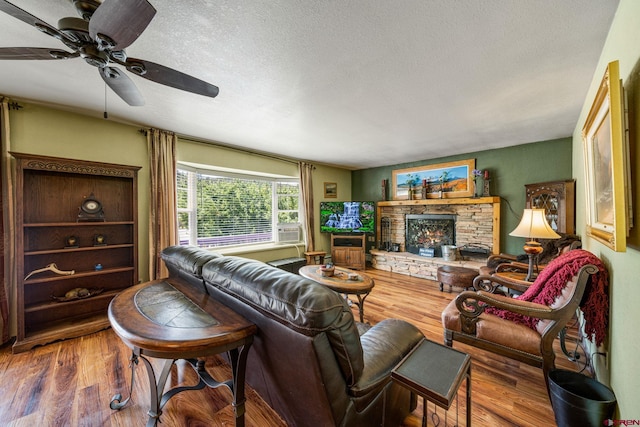 living room featuring ceiling fan, wood-type flooring, a textured ceiling, and a stone fireplace