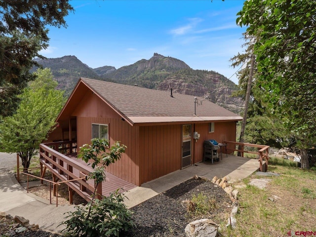 rear view of property with a shingled roof, a patio area, and a mountain view