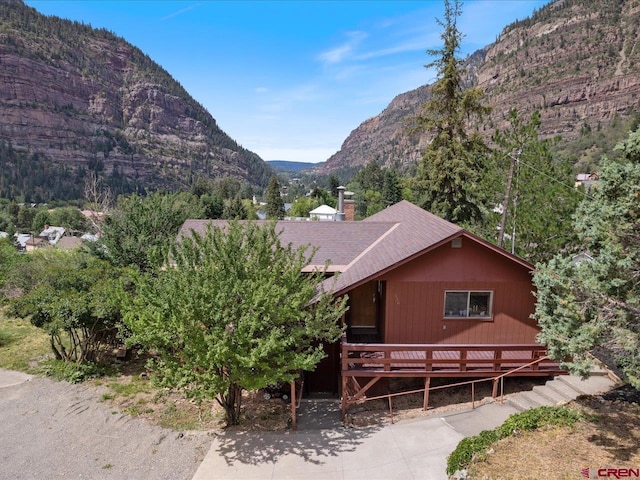 view of front of home with a deck with mountain view, concrete driveway, roof with shingles, and a chimney