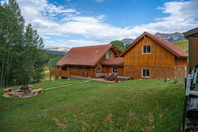 rear view of house featuring a lawn, an outdoor fire pit, a deck with mountain view, and a patio