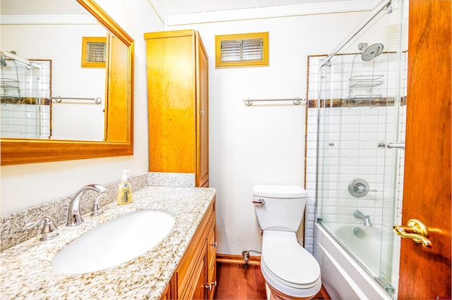 full bathroom featuring hardwood / wood-style floors, vanity, bath / shower combo with glass door, toilet, and ornamental molding