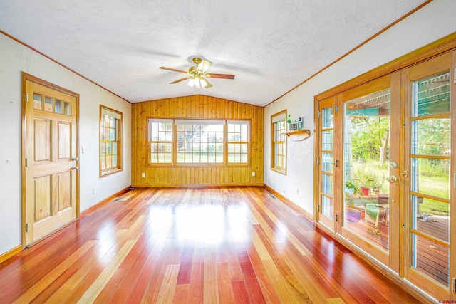 interior space featuring wooden walls, a healthy amount of sunlight, a textured ceiling, and light wood-type flooring