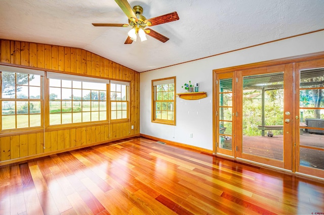 unfurnished room with wood walls, plenty of natural light, and light wood-type flooring