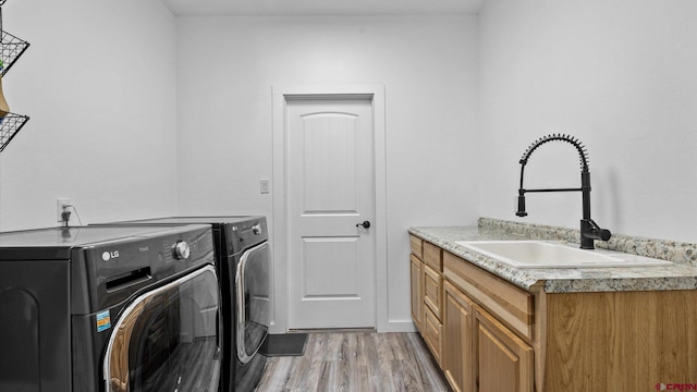 clothes washing area featuring sink, light wood-type flooring, cabinets, and washer and clothes dryer