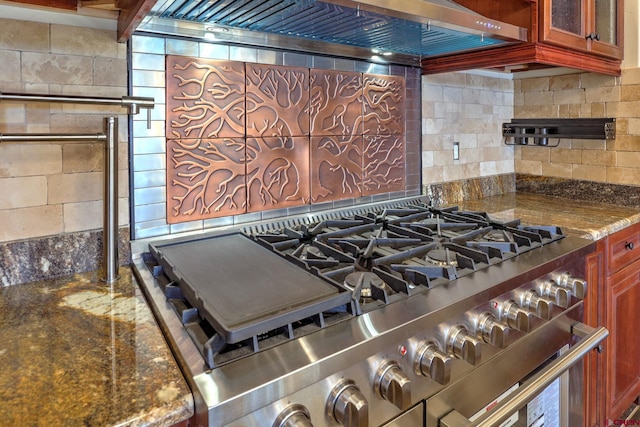 interior details featuring decorative backsplash, glass insert cabinets, dark stone countertops, high end stainless steel range, and wall chimney range hood