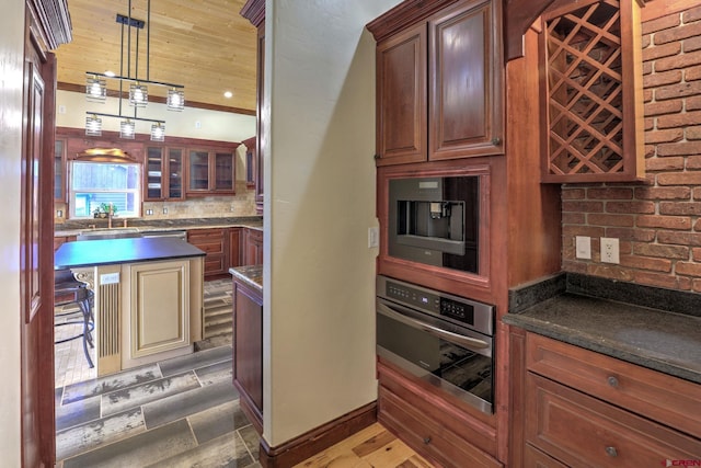 kitchen featuring decorative backsplash, dark countertops, glass insert cabinets, stainless steel oven, and pendant lighting