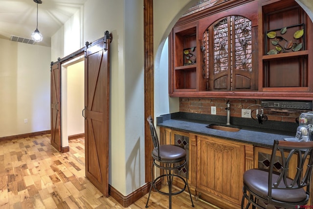 bar featuring visible vents, hanging light fixtures, a barn door, light wood-style floors, and a sink