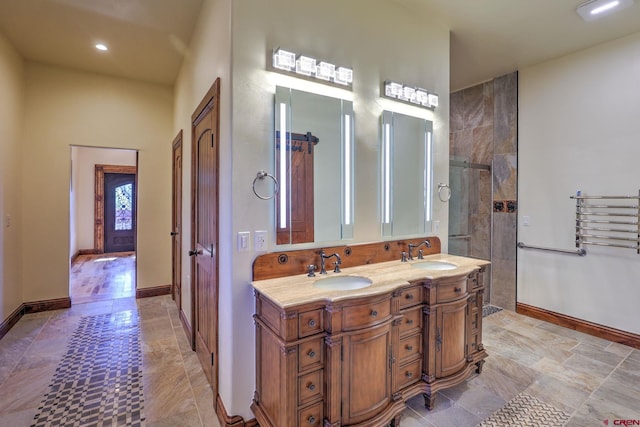 bathroom with a tile shower, double vanity, a sink, and baseboards