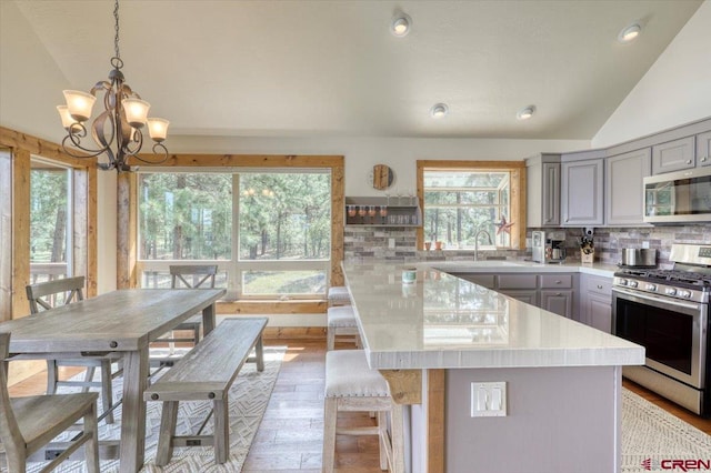 kitchen with gray cabinetry, stainless steel appliances, lofted ceiling, and tasteful backsplash