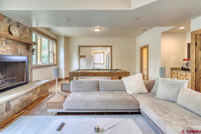 living room featuring hardwood / wood-style flooring, a stone fireplace, and pool table