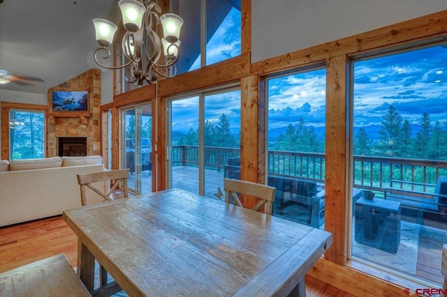 dining room featuring a mountain view, a fireplace, high vaulted ceiling, ceiling fan with notable chandelier, and hardwood / wood-style flooring