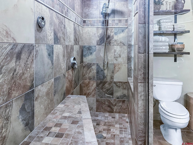 bathroom with tiled shower, toilet, and tile patterned flooring