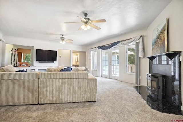 carpeted living room featuring a wood stove, ceiling fan, a wealth of natural light, and french doors