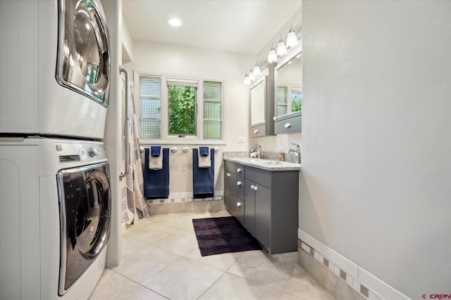 laundry area with stacked washer and dryer, light tile patterned flooring, a sink, and baseboards