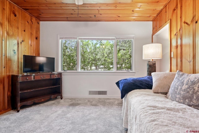 carpeted bedroom with wood ceiling, visible vents, and wooden walls