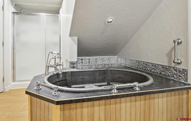 bathroom with a textured wall, a stall shower, a textured ceiling, wood finished floors, and a bath