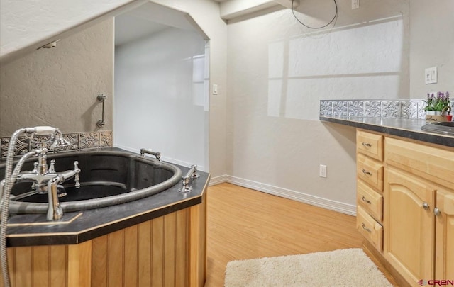 kitchen with arched walkways, light wood-style flooring, a sink, baseboards, and dark countertops