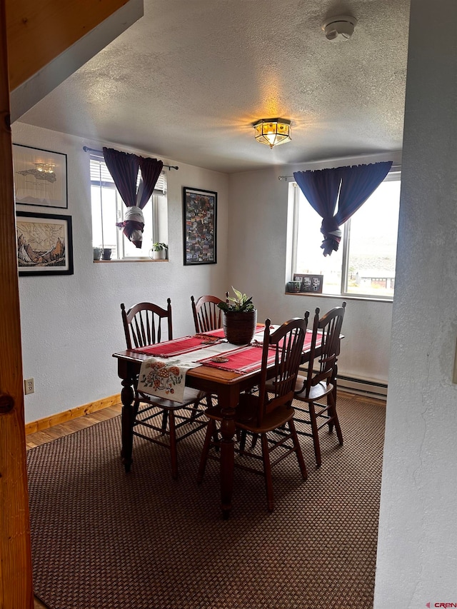 carpeted dining space with a textured ceiling and baseboard heating