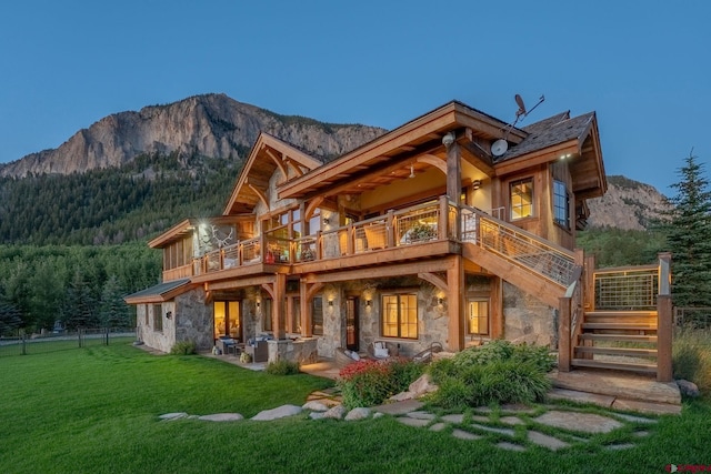 back of house with a lawn, a mountain view, and a balcony