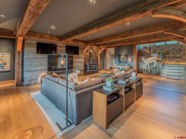 living room featuring a wood stove, light hardwood / wood-style floors, and beam ceiling