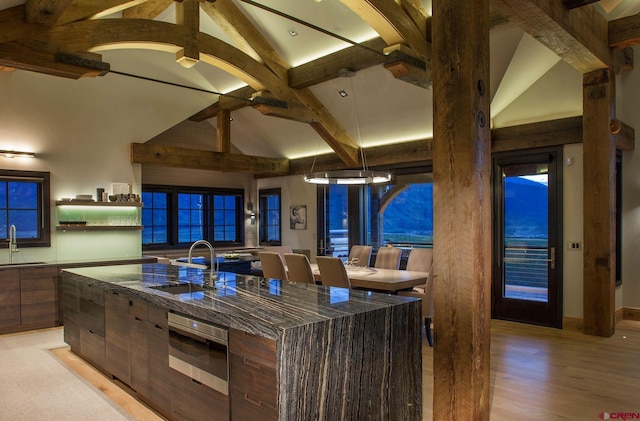 kitchen with light hardwood / wood-style flooring, appliances with stainless steel finishes, beamed ceiling, sink, and a center island with sink