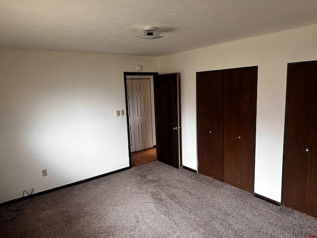 unfurnished bedroom featuring multiple closets, a textured ceiling, and dark colored carpet