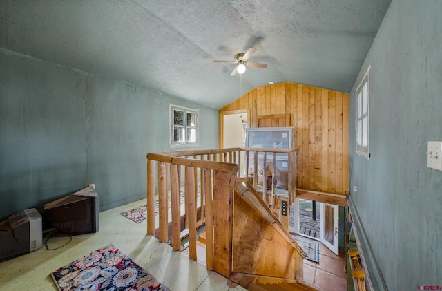 interior space featuring wood walls, ceiling fan, a textured ceiling, and vaulted ceiling