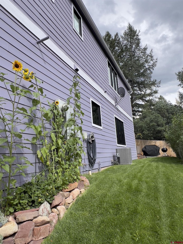 view of side of property featuring central air condition unit, a lawn, and fence