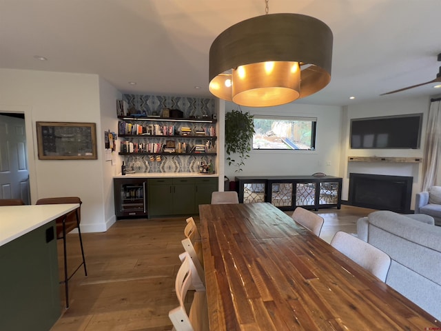 dining area with beverage cooler, a ceiling fan, hardwood / wood-style floors, a fireplace, and a dry bar