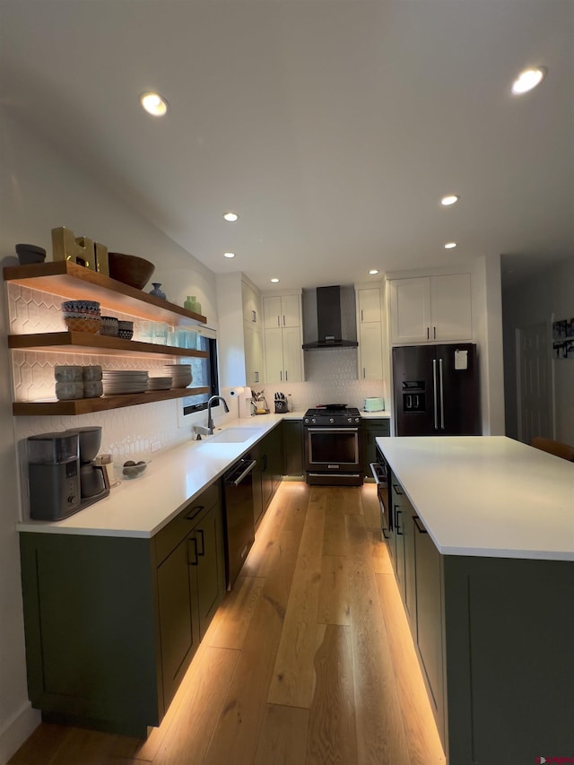 kitchen featuring light wood-style flooring, white cabinets, black appliances, wall chimney exhaust hood, and a sink