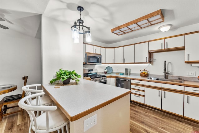 kitchen with white cabinets, hanging light fixtures, stainless steel appliances, and sink