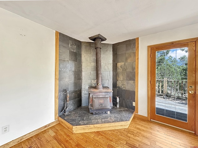 interior details with a wood stove, a textured ceiling, baseboards, and wood finished floors