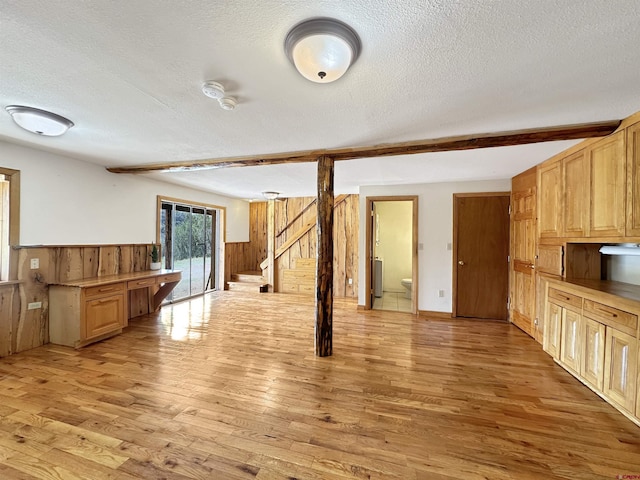 interior space featuring a textured ceiling, wooden walls, a wainscoted wall, light wood-type flooring, and beamed ceiling