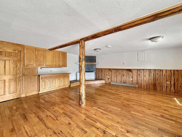 unfurnished living room featuring beam ceiling, light wood-style flooring, baseboard heating, wainscoting, and a textured ceiling