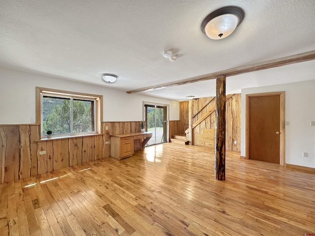 spare room featuring a wainscoted wall, stairway, light wood-style floors, wooden walls, and a textured ceiling