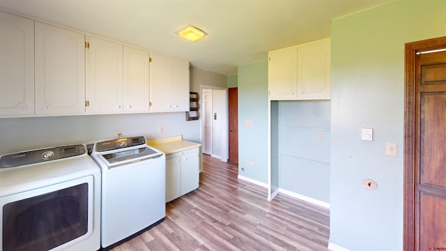 clothes washing area featuring separate washer and dryer, light hardwood / wood-style flooring, and cabinets