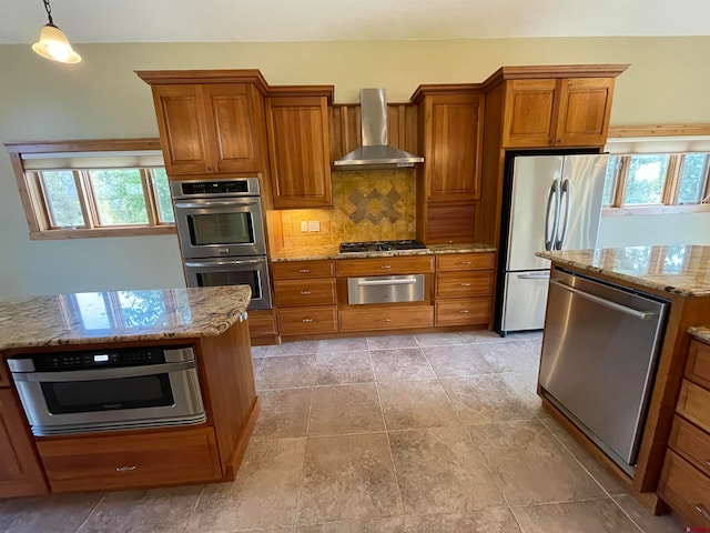 kitchen featuring wall chimney range hood, appliances with stainless steel finishes, a wealth of natural light, and decorative light fixtures