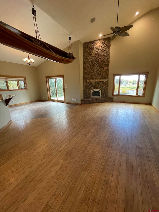 unfurnished living room featuring hardwood / wood-style floors, ceiling fan with notable chandelier, beamed ceiling, and a stone fireplace