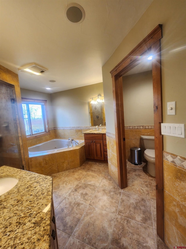 bathroom with vanity, tiled bath, tile patterned flooring, tile walls, and toilet