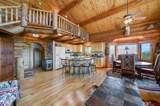 dining area with beamed ceiling, light hardwood / wood-style flooring, rustic walls, ceiling fan, and wood ceiling